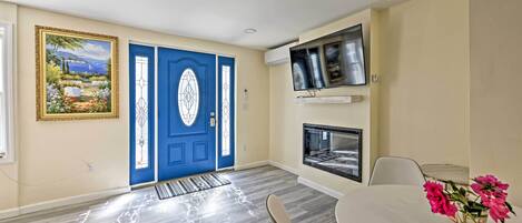 Una habitación con puerta azul, un cuadro, un televisor y una chimenea.