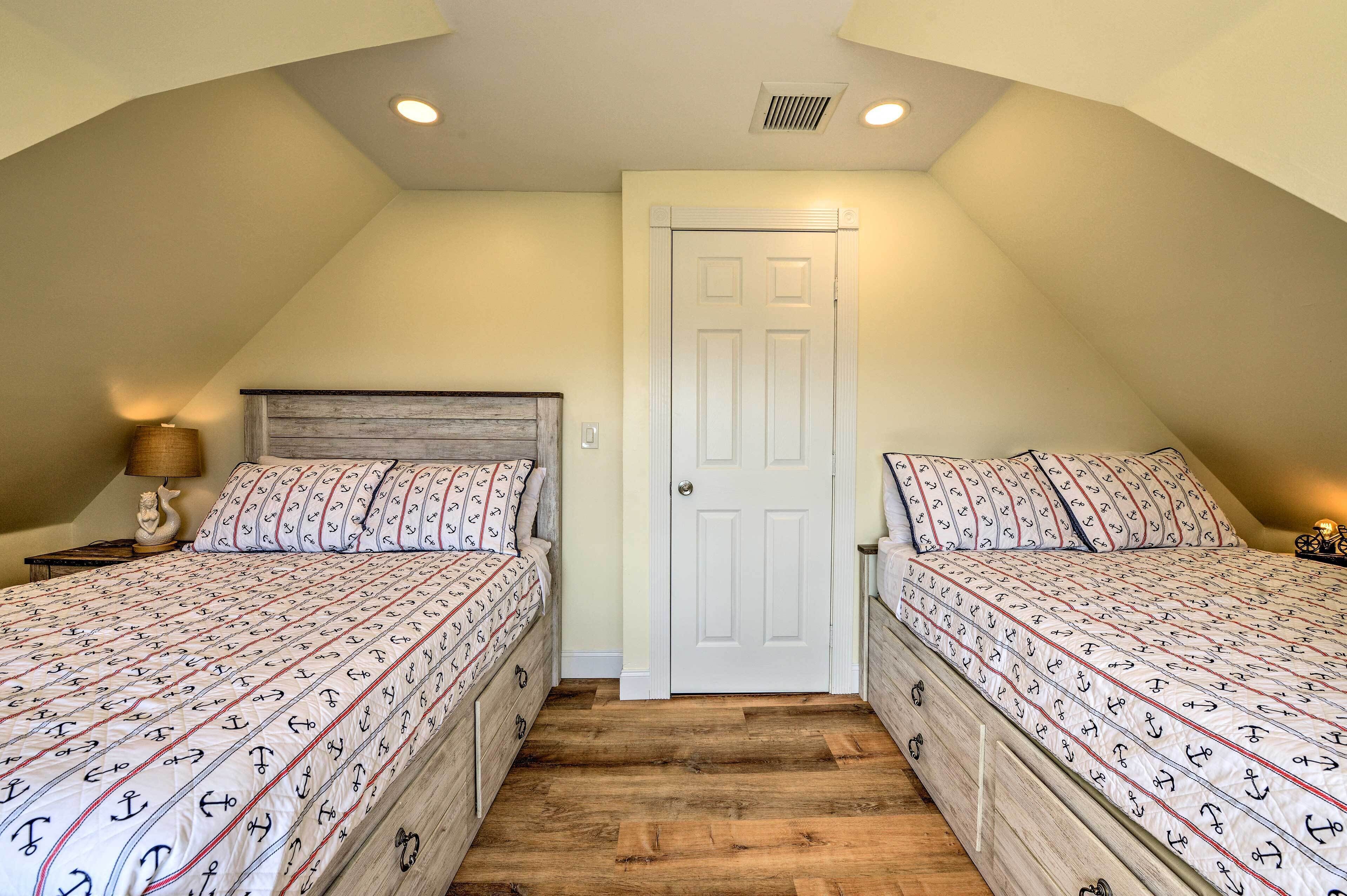A bedroom with two beds, wooden flooring, a white door, and a lamp on a nightstand.