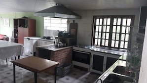 Une cuisine équipée d’un poêle en briques, d’une cuisinière à gaz, d’un évier et d’une fenêtre donnant sur un paysage verdoyant.