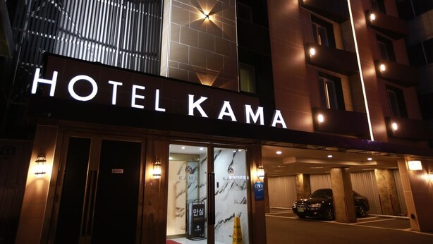 Exterior del Hotel KAMA de noche, con señalización iluminada y fachada moderna.