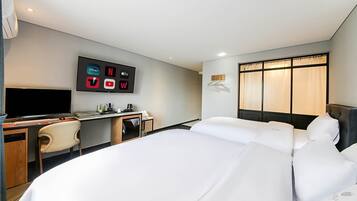 A hotel room with a large bed, a desk with a flat-screen TV, and a wall-mounted TV displaying streaming service logos.