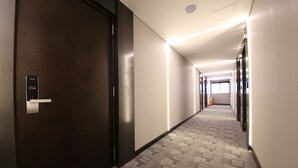 Un pasillo de hotel con piso alfombrado, una puerta con cerradura y un accesorio de iluminación en el techo.