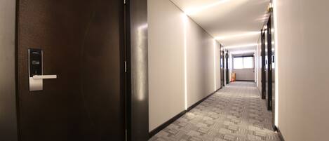 A hotel hallway with a carpeted floor, a door with a lock, and a light fixture on the ceiling.