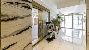 Un interior moderno con una pared de mármol, un acceso por puerta de cristal y un expositor promocional.