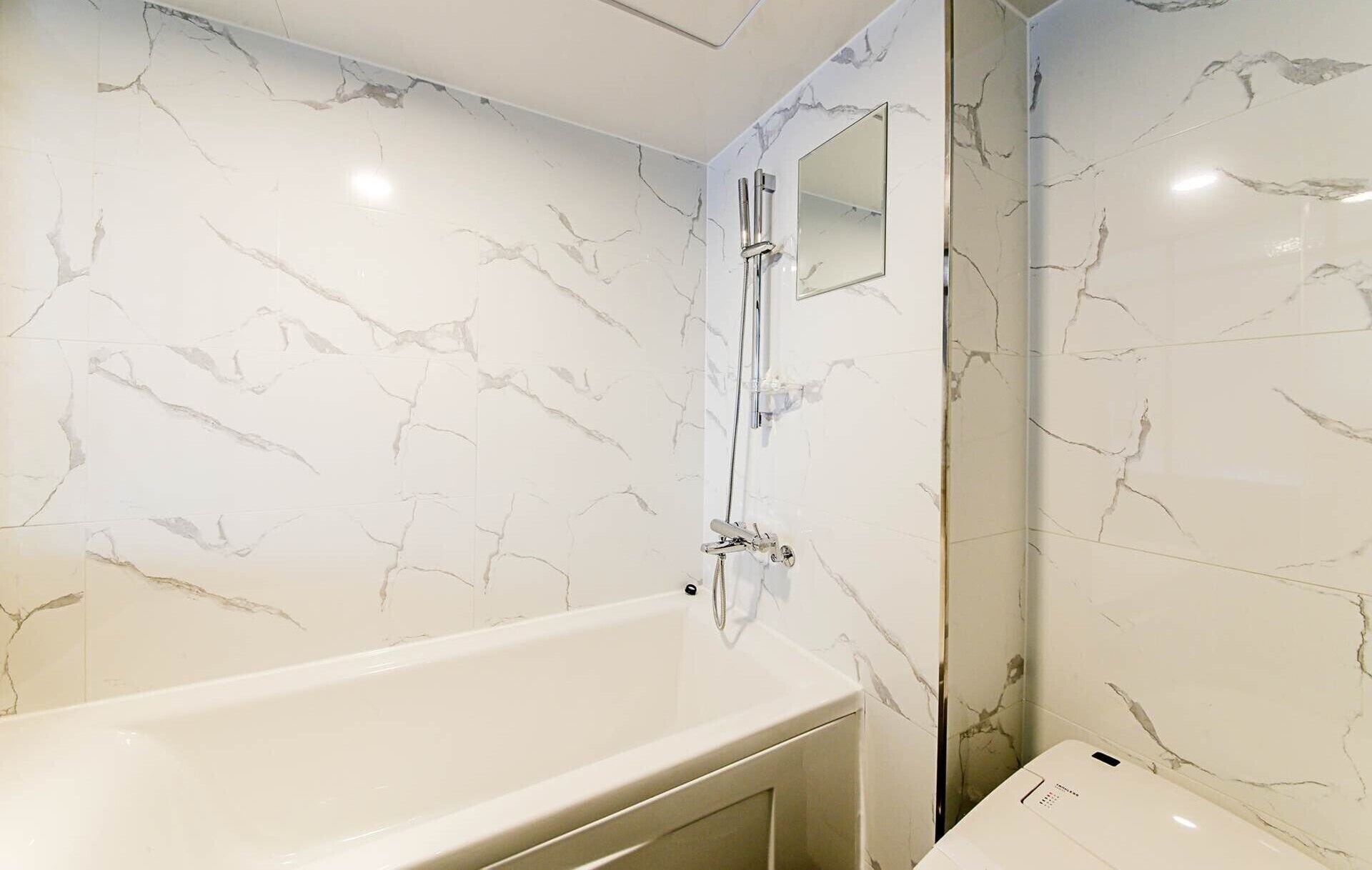 Un baño con pared de mármol blanco, una bañera y una ducha.