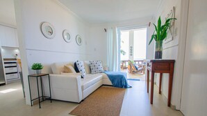 Ein modernes Wohnzimmer mit einem weißen Sofa, einem kleinen Beistelltisch mit einer Pflanze und einem Holzstuhl.