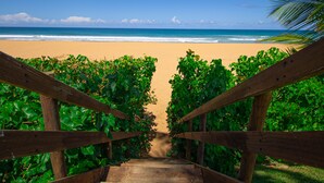 Eine Holztreppe führt zu einem Strand, gesäumt von üppigem Grün.