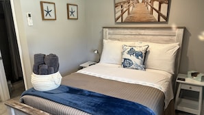 A neatly made bed with a headboard, a bedside table with a lamp, and a wall-mounted artwork. - Serenity By The River beach 🏖️ gateway  (Edgewater)