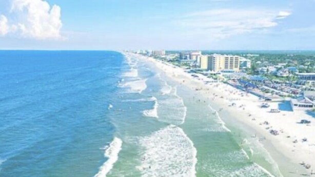 An aerial view of a beach with a long stretch of shoreline, buildings, and a clear sky. - Serenity By The River beach 🏖️ gateway  (Edgewater)