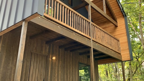 Une cabane moderne en bois, à deux étages, dotée d’un balcon et située dans une zone boisée.