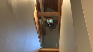 Un escalier en bois muni d’une rampe, menant à un palier où est fixée une applique murale.