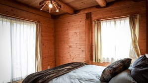 Un dormitorio de cabaña de madera con una cama, cortinas y una lámpara colgante.