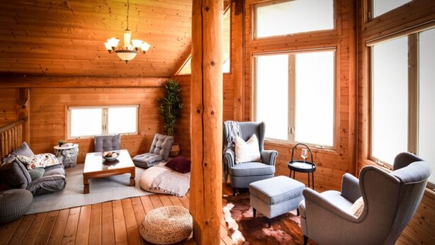 Un acogedor interior de cabaña de madera con un conjunto de sofá, una mesa de centro, una silla y una alfombra.
