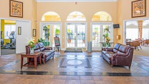A spacious lobby with a high ceiling, a central seating area with leather sofas, a tiled floor, and a view of the outdoor patio through arched windows.
