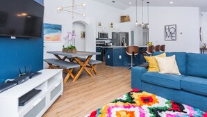 A modern living room with a blue sofa, a colorful rug, and a TV on a white stand.