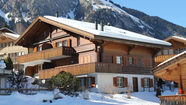 Un edificio de estilo chalé con fachada de madera, varios balcones y techo cubierto de nieve.