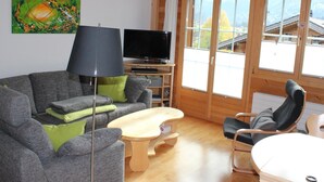 Una sala de estar acogedora con un sofá gris, una pequeña mesa de madera, una lámpara de pie negra y un televisor sobre un mueble de madera.