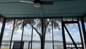 Une pièce dotée d’un ventilateur de plafond, de grandes fenêtres et offrant une vue sur un lac avec un quai.
