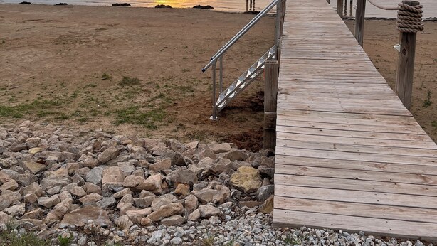 Une jetée en bois s’étendant sur une étendue d’eau calme, avec un coucher de soleil en arrière-plan.