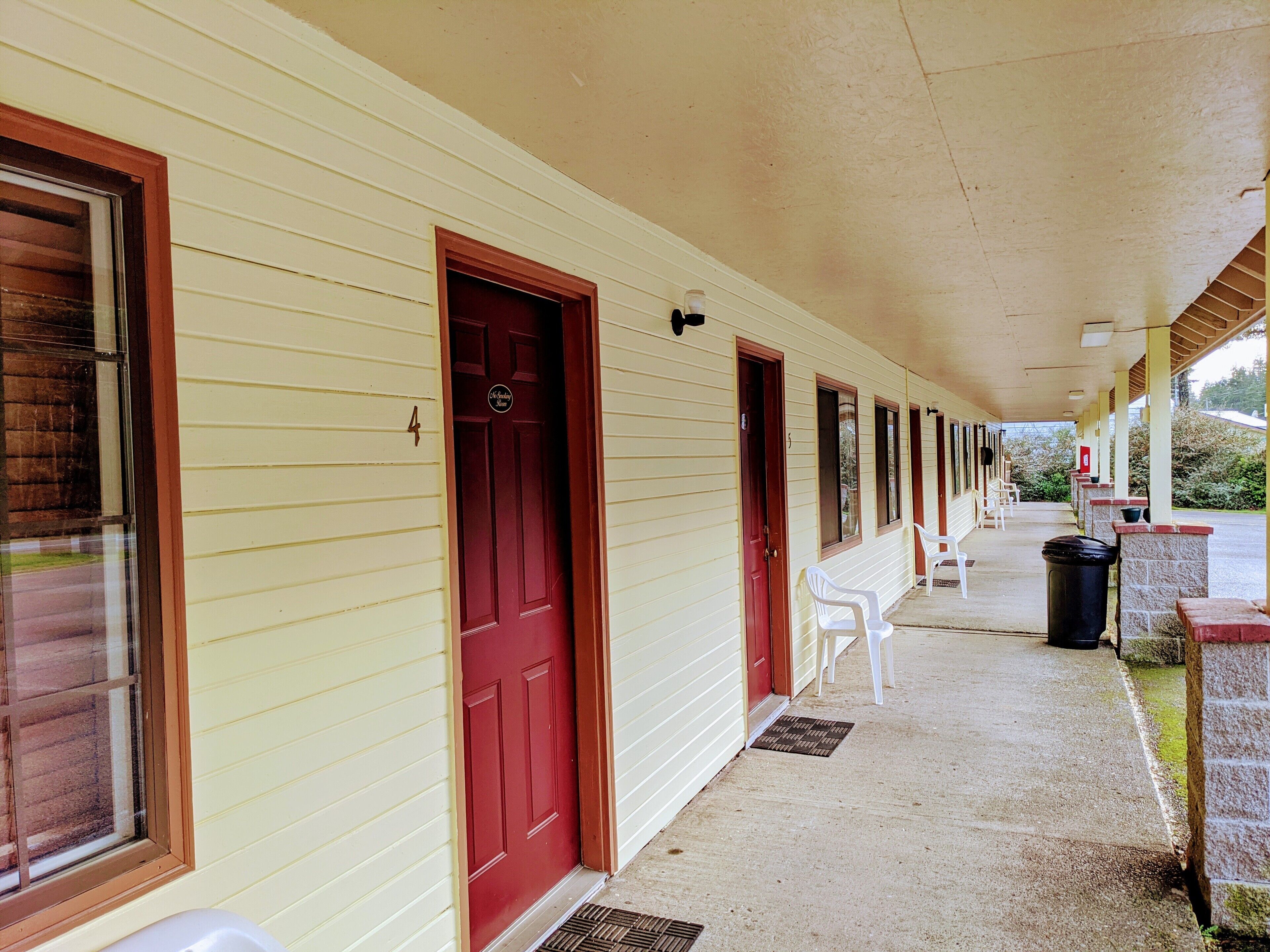 A motel with a covered porch, multiple doors, and a row of white plastic chairs.