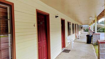 A motel with a covered porch, multiple doors, and a row of white plastic chairs.