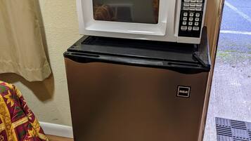 A compact refrigerator with a microwave on top, a control panel, and a small logo on the door.