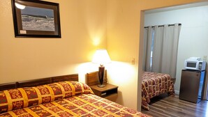 A hotel room with two beds, a nightstand with a lamp, a microwave, and a framed picture on the wall.