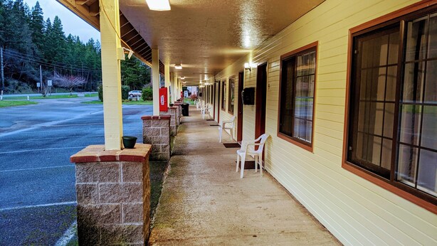 A covered corridor with a row of single windows, a concrete floor, and a row of white plastic chairs.