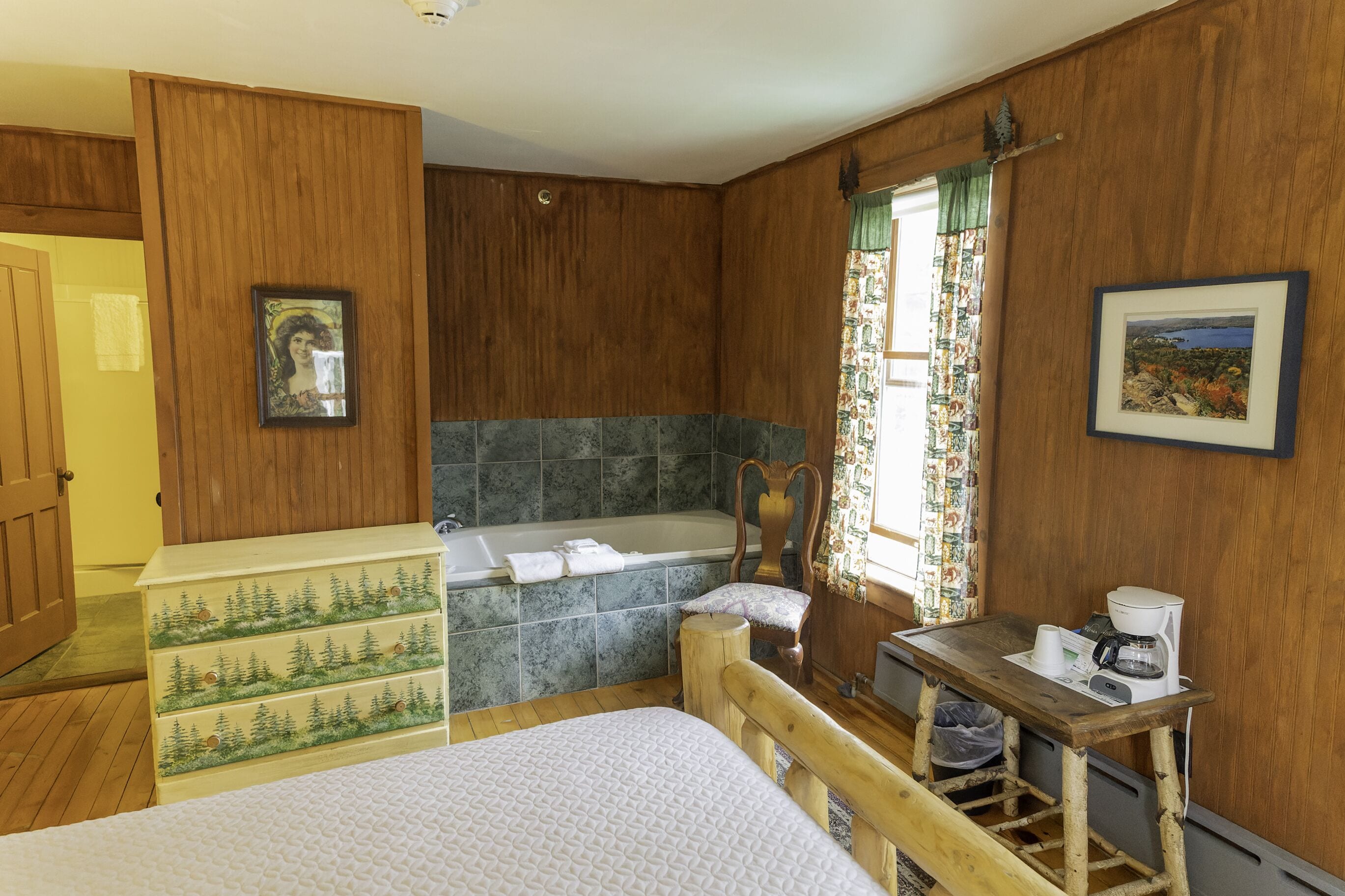 A wooden-paneled bathroom with a bathtub, a wooden dresser, and a small table with a coffee maker.