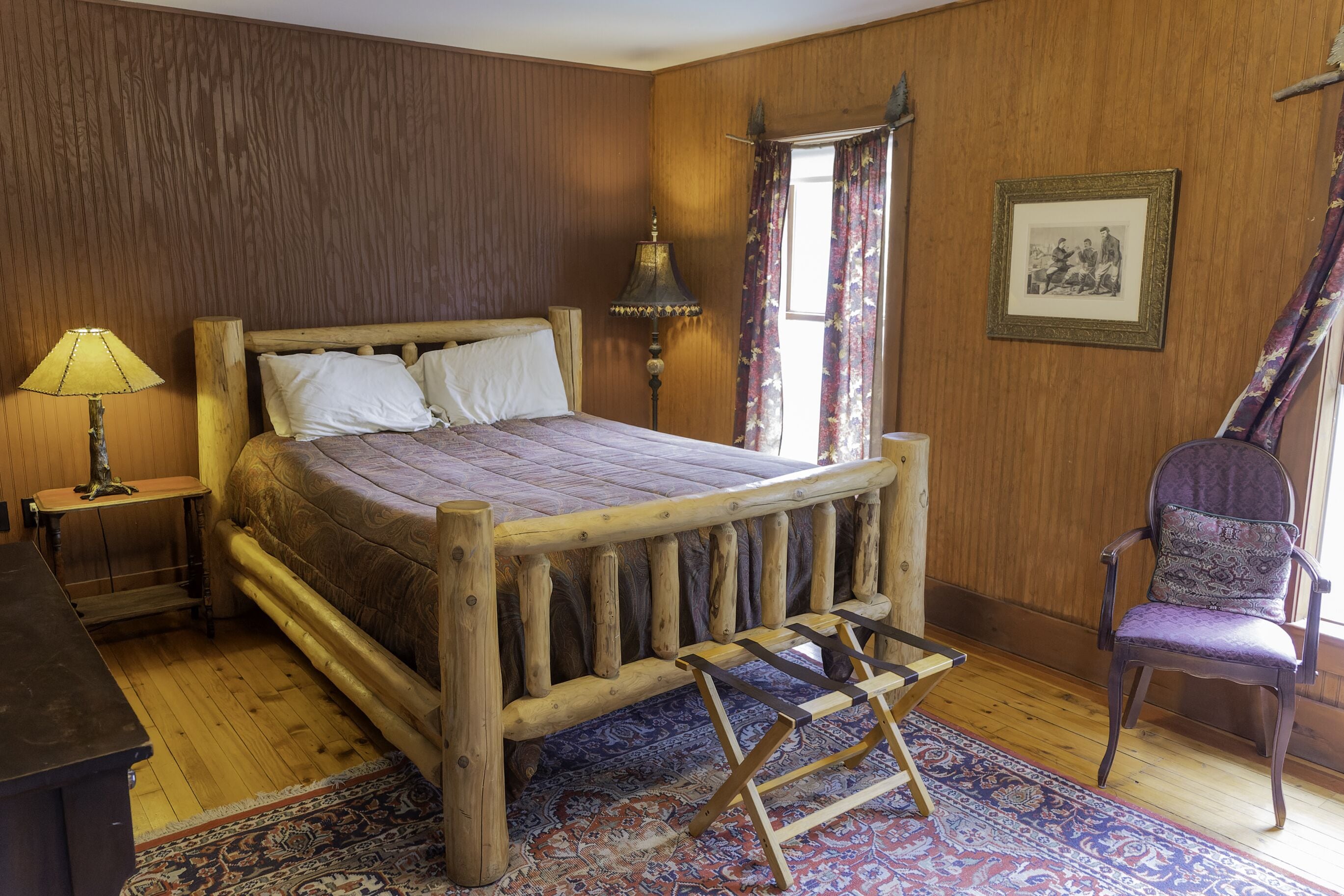A wooden bed with a headboard, a nightstand with a lamp, a chair, and a patterned rug.