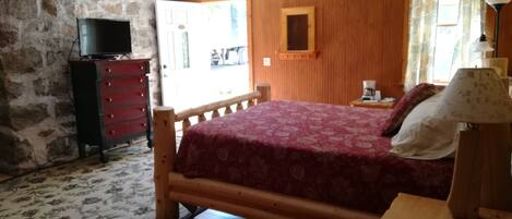 A bedroom with a wooden bed, a dresser, a television, and a window with curtains.
