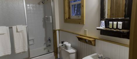 Un baño con ducha, inodoro, lavabo y una ventana sobre el espejo.