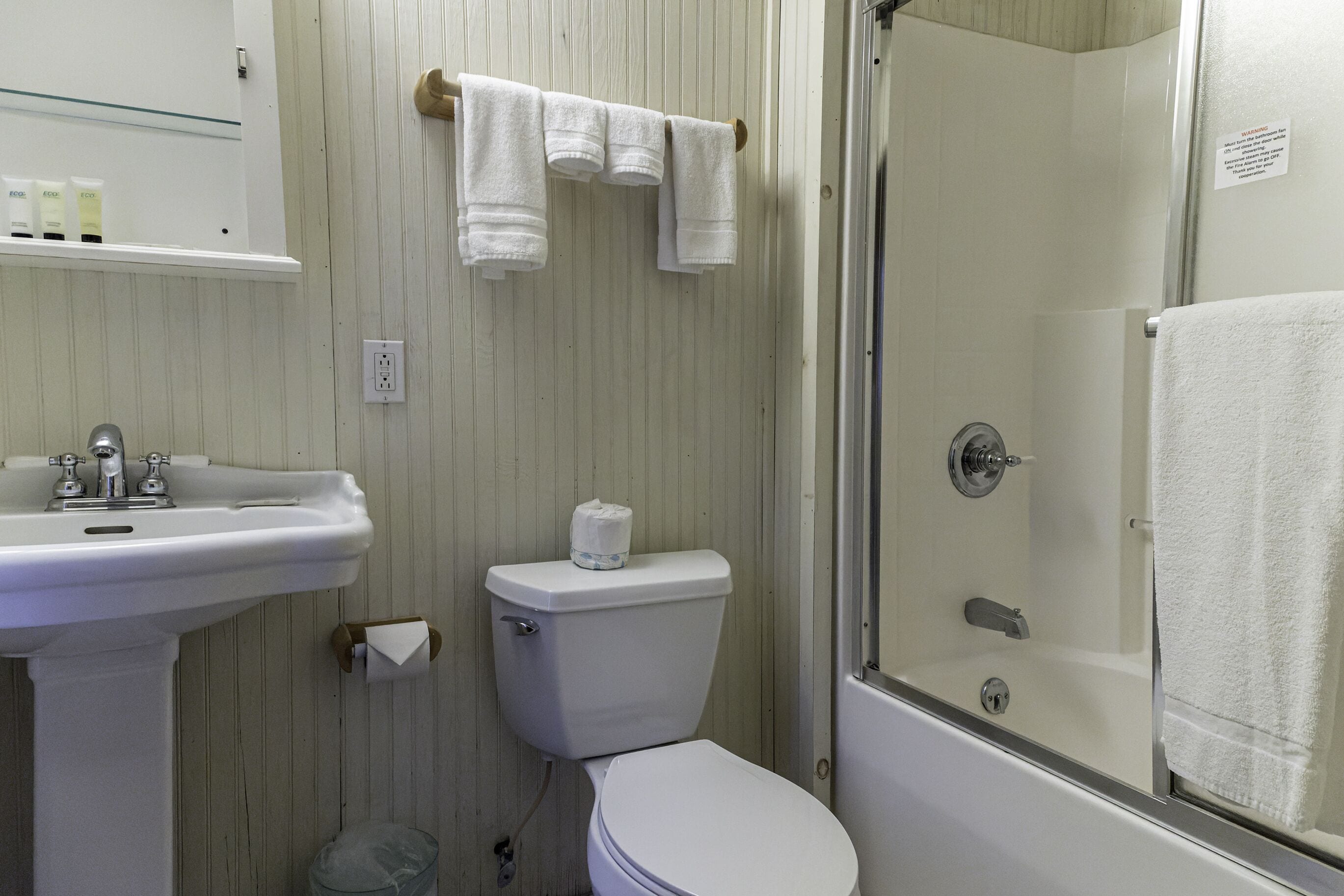 Un baño con lavamanos, inodoro y ducha. Hay toallas colgadas en un perchero.
