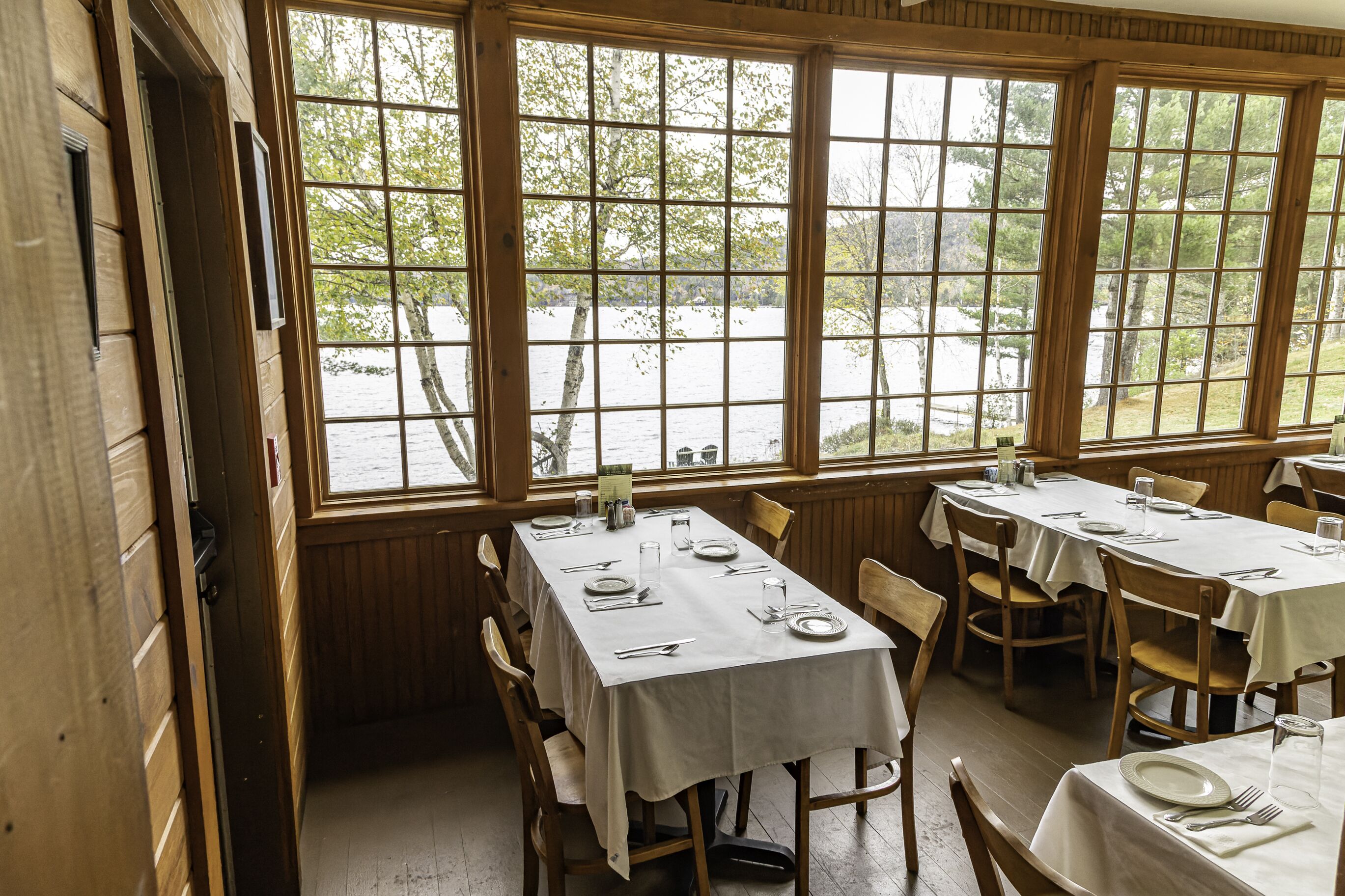 A dining area with large windows, wooden walls, and tables set for dining.