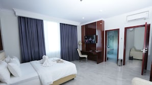 A hotel room with a bed, a desk, a TV, and a bathroom visible through an open door. - Sindoro Hotel Cilacap by Conary (Cilacap)