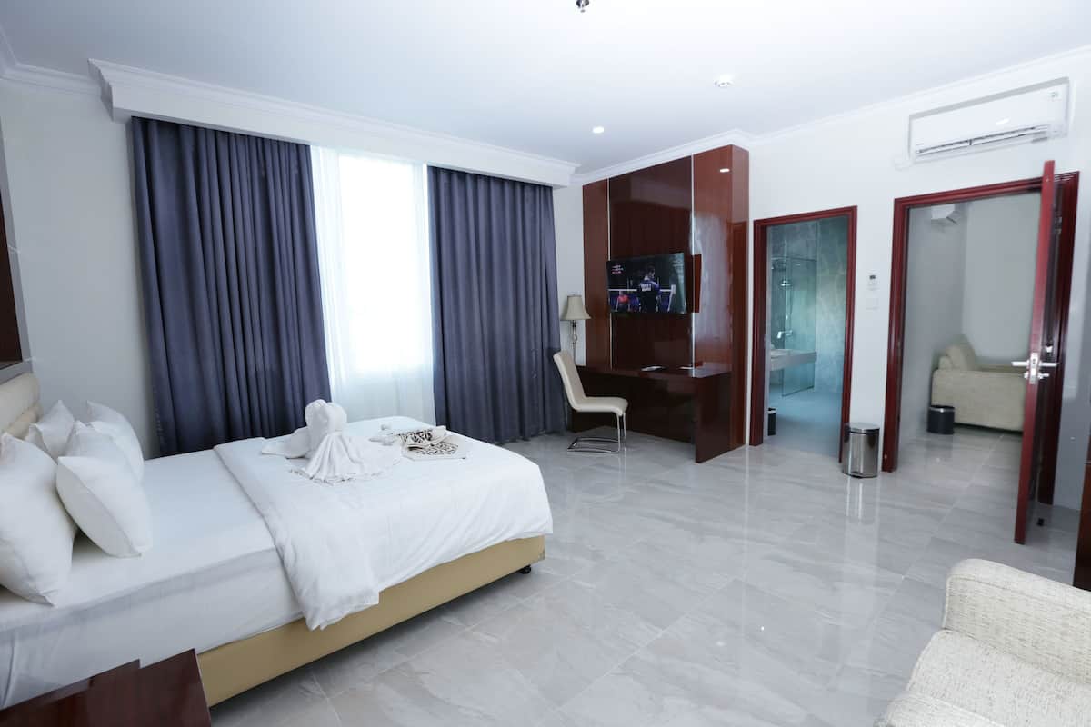 Habitación de hotel con cama, escritorio, televisor y baño visible a través de una puerta abierta.