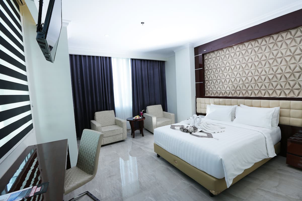 Una habitación de hotel con una cama grande, dos sillones, una mesita con frutero y un televisor montado en la pared.