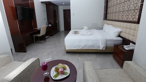 A hotel room with a bed, bedside table, TV, and a dining area with a table and chairs. - Sindoro Hotel Cilacap by Conary (Cilacap)