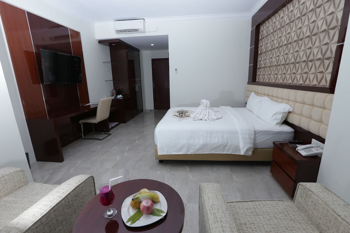 Habitación de hotel con cama, mesita de noche, televisión y zona de comedor con mesa y sillas.