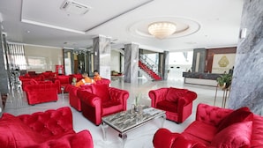 A spacious lobby with red sofas and a marble coffee table, a reception desk, and a staircase. - Sindoro Hotel Cilacap by Conary (Cilacap)