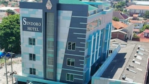A modern hotel with a prominent sign, multiple parking spaces, and a view of the surrounding area. - Sindoro Hotel Cilacap by Conary (Cilacap)