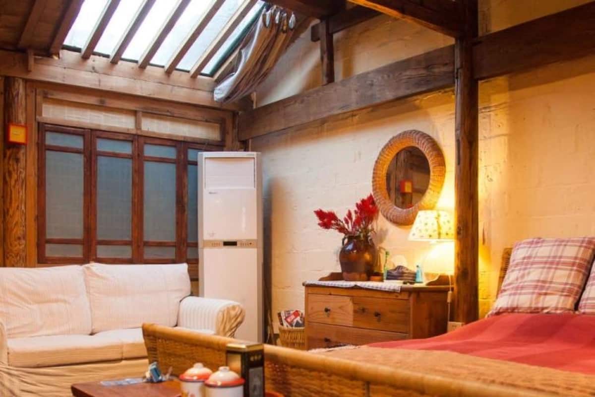 Une pièce confortable avec un lit, un canapé, une table en bois sur laquelle se trouve un plateau avec divers objets, un miroir et une fenêtre à vitre dépolie.