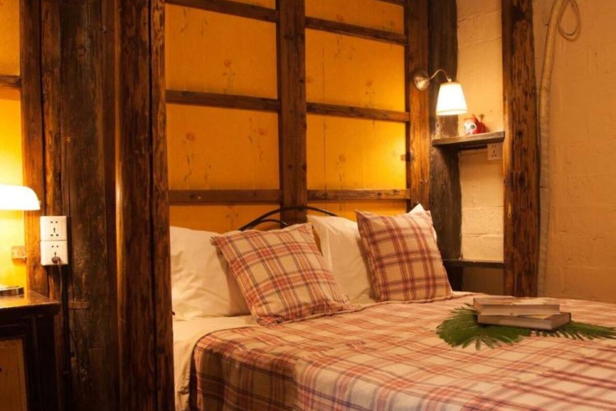 Une chambre chaleureuse avec une tête de lit en bois, un lit recouvert d’une couette à carreaux, une lampe de chevet et une petite étagère ornée d’un objet décoratif.