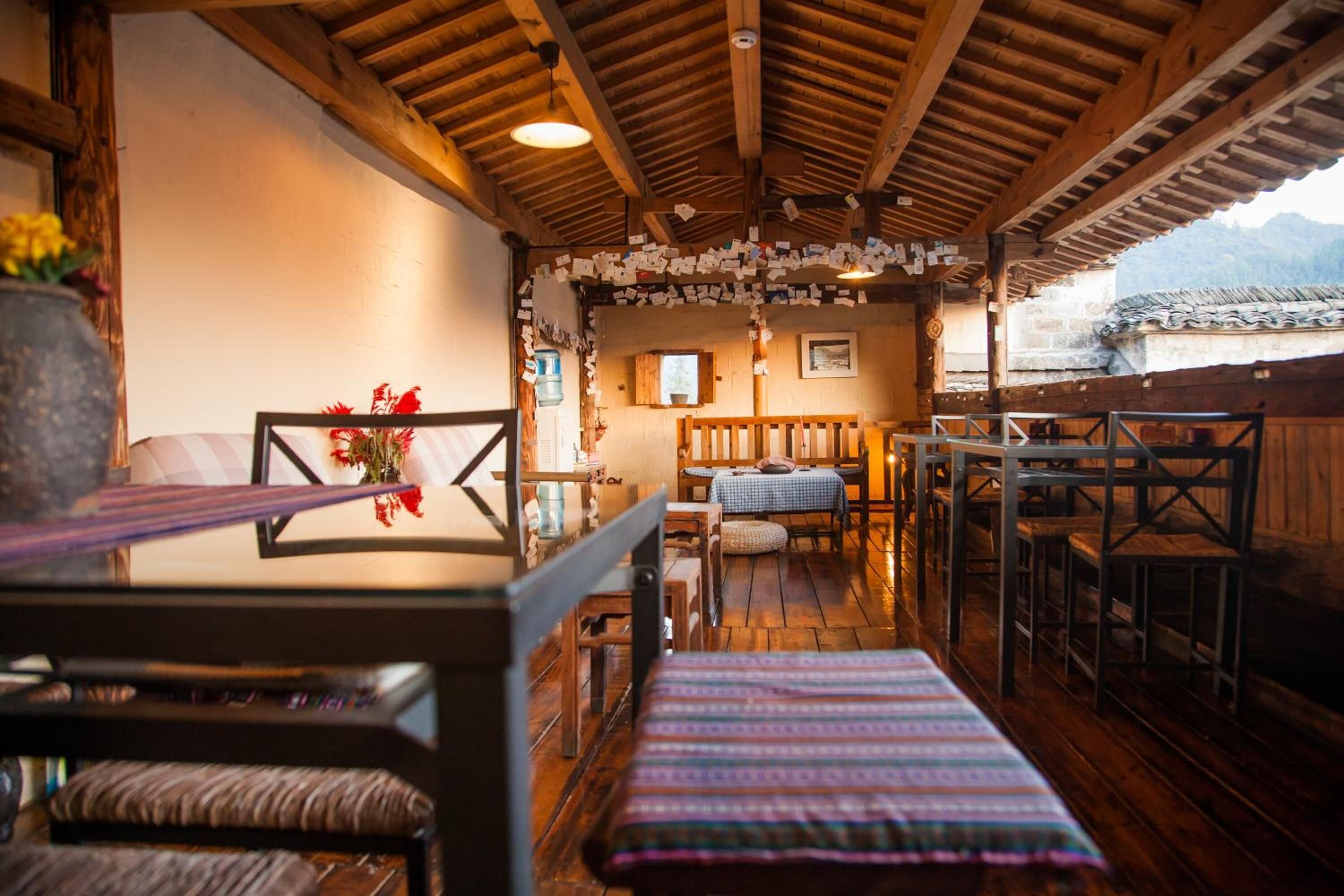 A rustic wooden interior with a long table and benches, a small window, and a view of the outside.