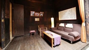 Um quarto aconchegante com piso de madeira, um sofá, uma cadeira, uma mesa pequena e uma parede decorada com quadros e uma grande obra de caligrafia.