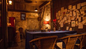 Uma área de jantar rústica com parede de pedra, móveis de madeira e uma mesa com abajur vermelho.