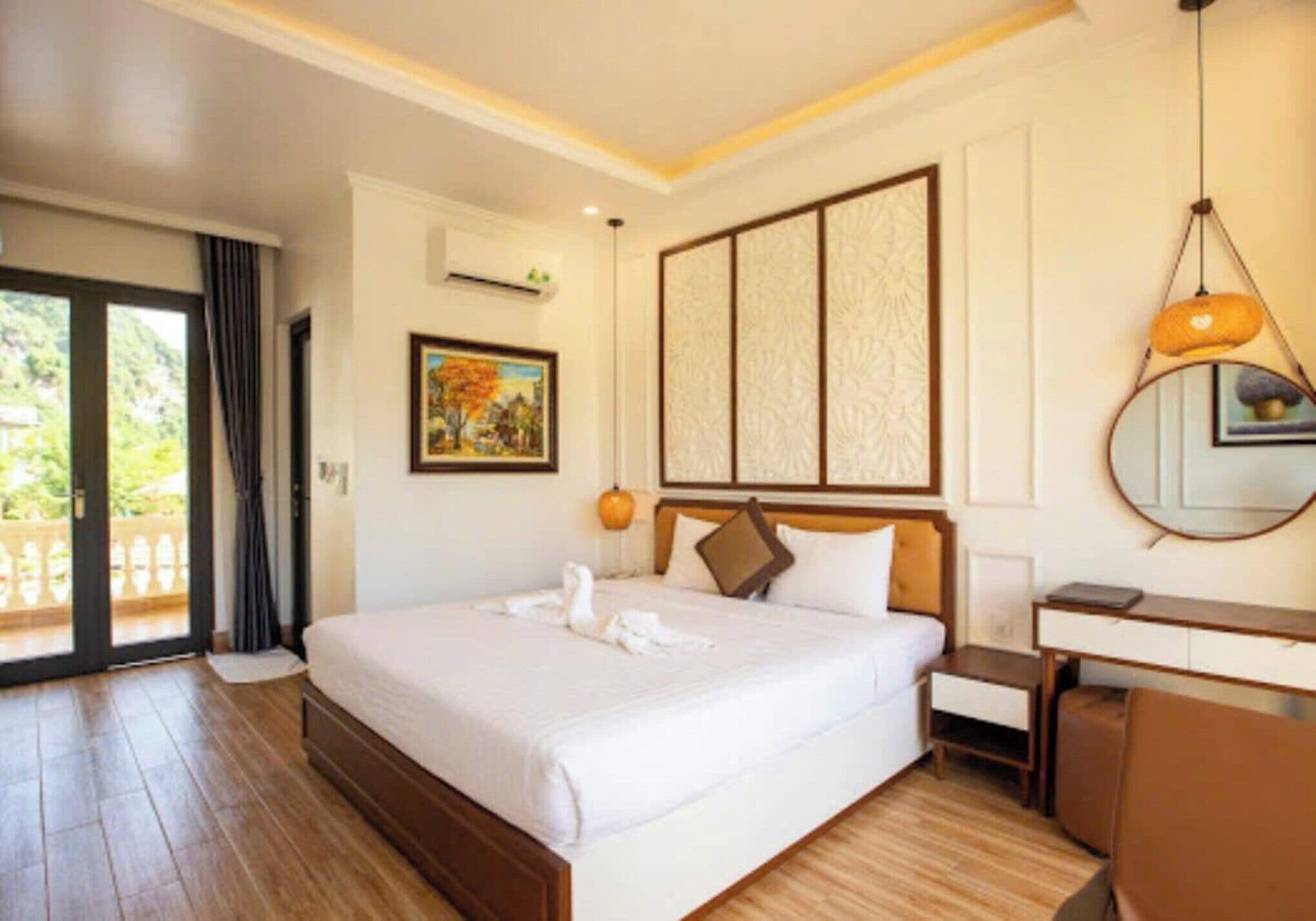 Habitación de hotel con una cama grande, un escritorio, una silla, un espejo y una puerta corrediza a un balcón.