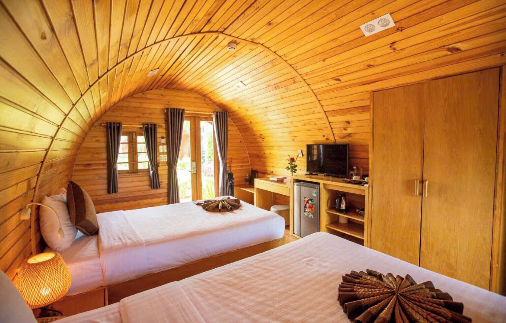 A cozy, wooden cabin room with two beds, a desk, a television, and a wardrobe.
