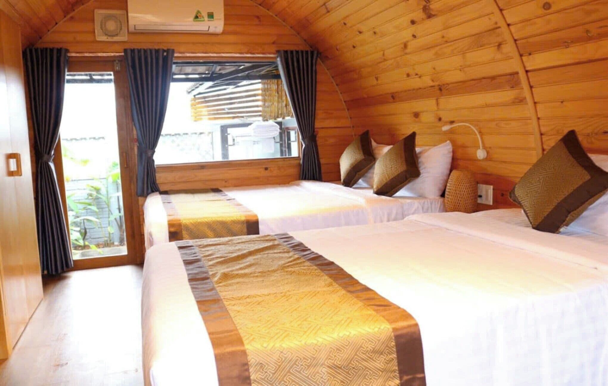 A cabin with two beds, wooden walls, a window with curtains, and an air conditioning unit.
