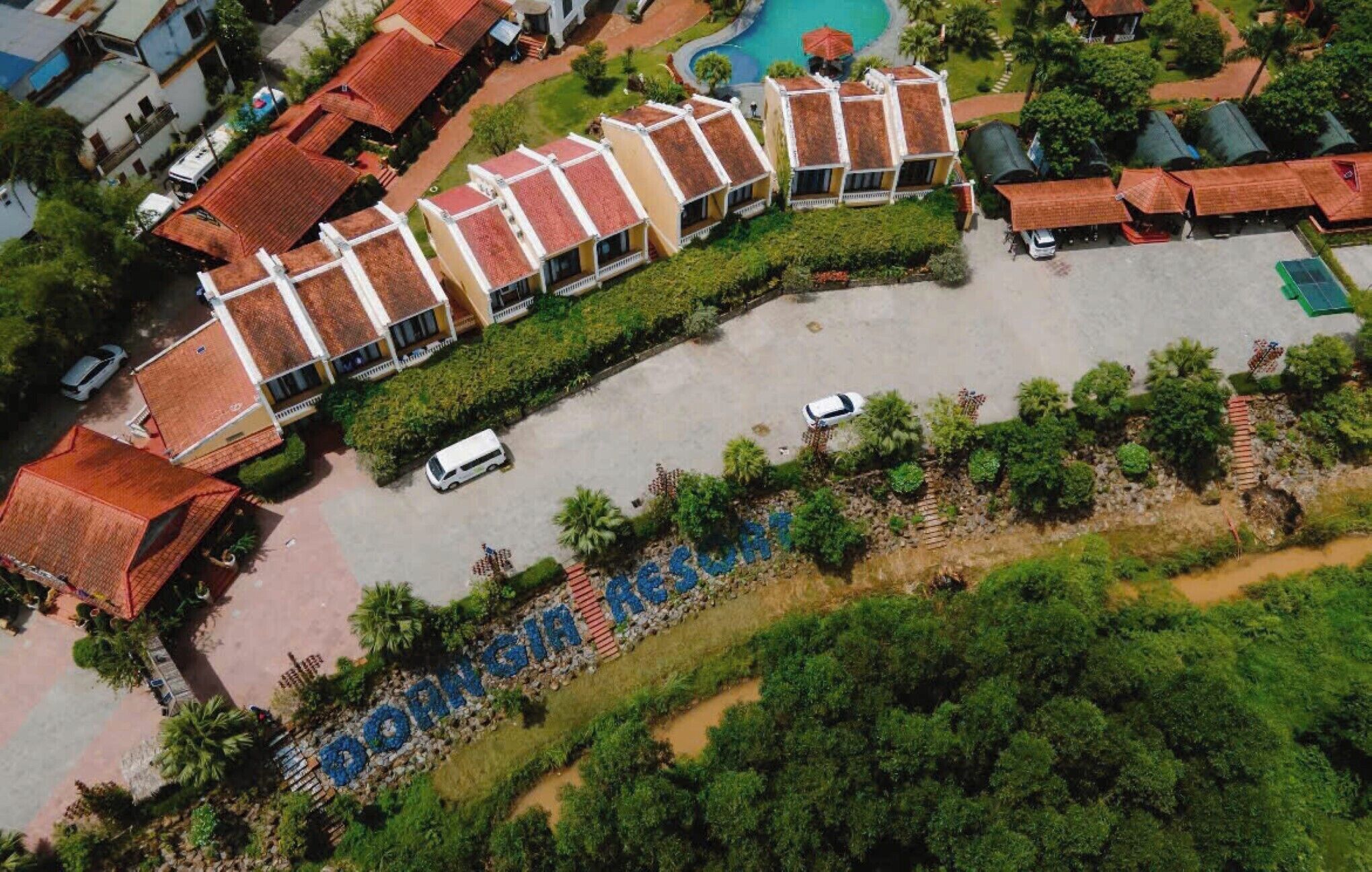 Eine Vogelperspektive zeigt ein Resort mit mehreren Gebäuden, einem Schwimmbad und einer gepflegten Landschaft.